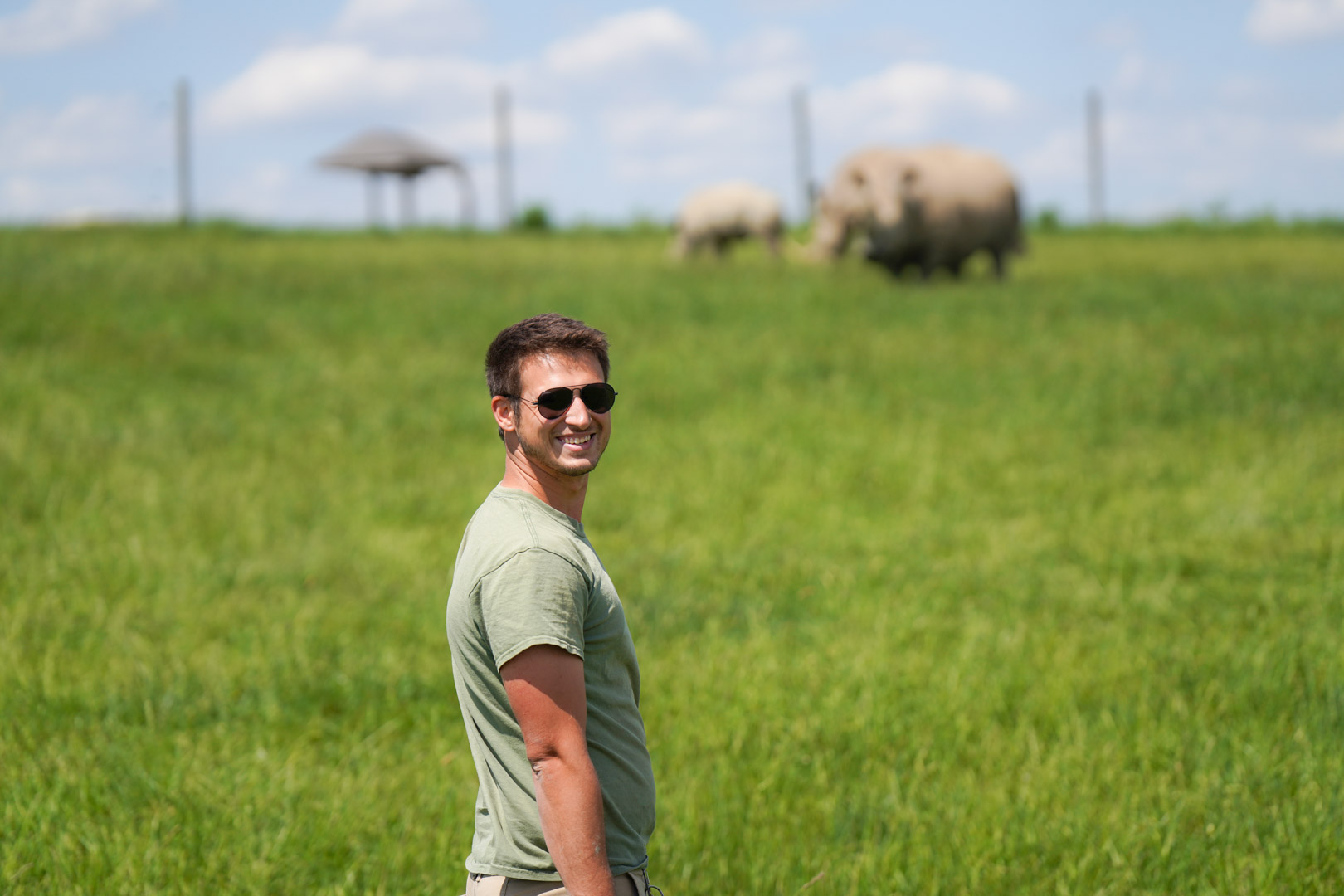 man standing in field with rhinos in the background